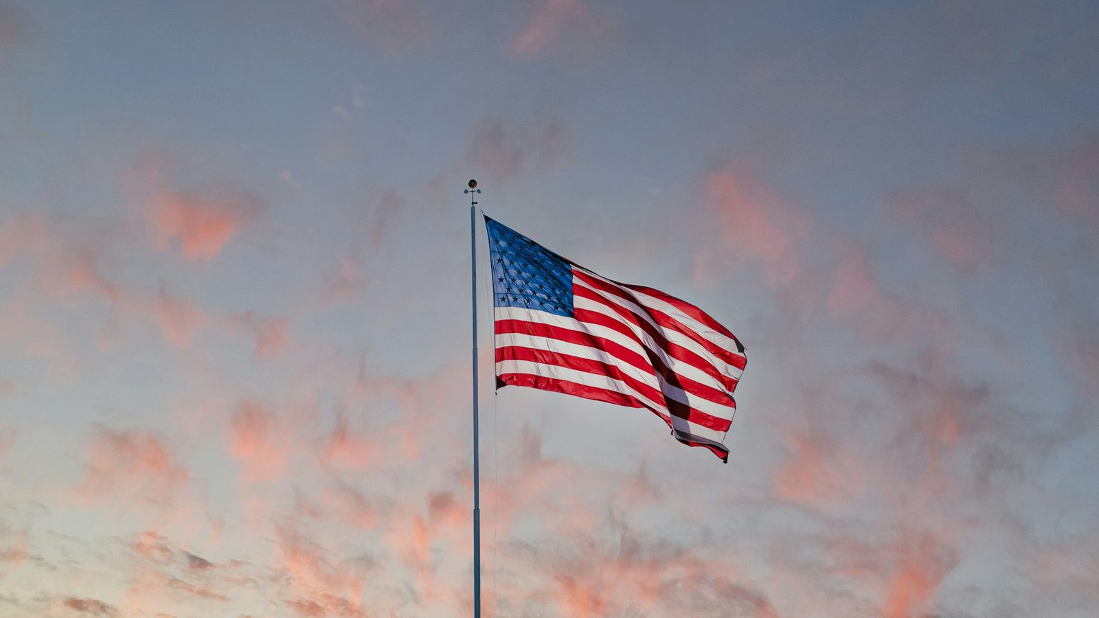 An American flag against a pink evening sky